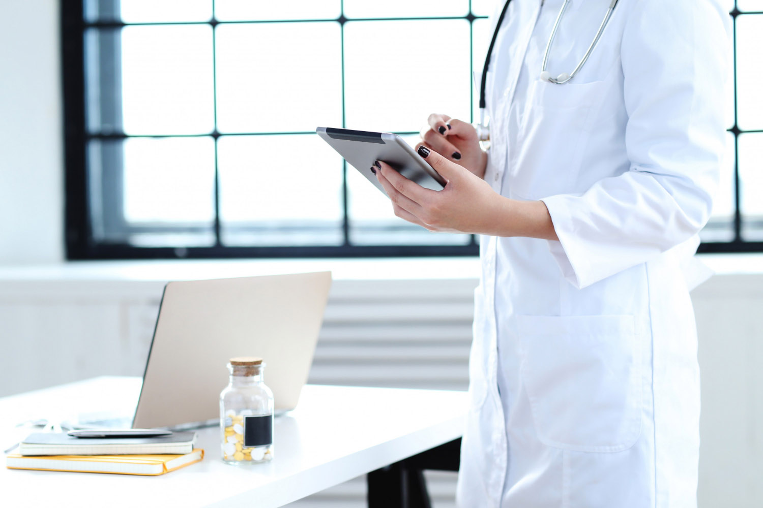 médico com um celular na mão e ao lado uma mesa com um notebook em cima ferramentas para gestão de consultório